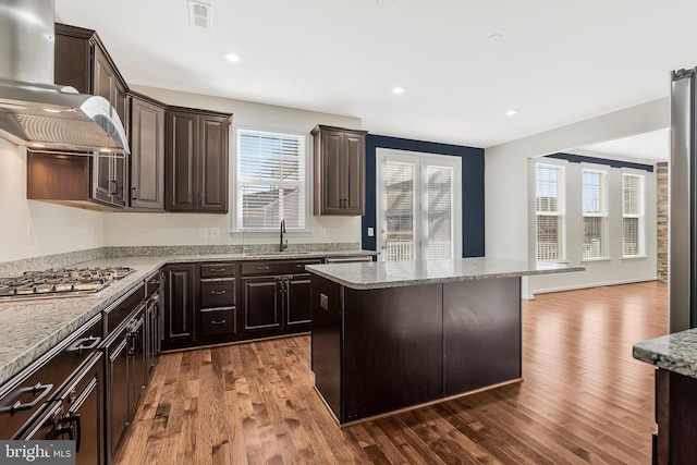 kitchen featuring a sink, wood finished floors, exhaust hood, a center island, and light stone countertops