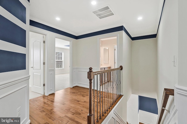 hall with ornamental molding, visible vents, an upstairs landing, and wood finished floors