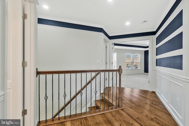 corridor with visible vents, ornamental molding, wood finished floors, an upstairs landing, and a decorative wall