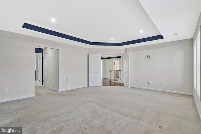 empty room with visible vents, a tray ceiling, baseboards, and light colored carpet