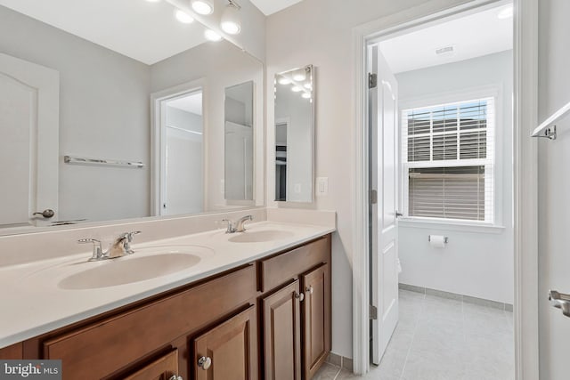 full bath with double vanity, tile patterned flooring, a sink, and baseboards