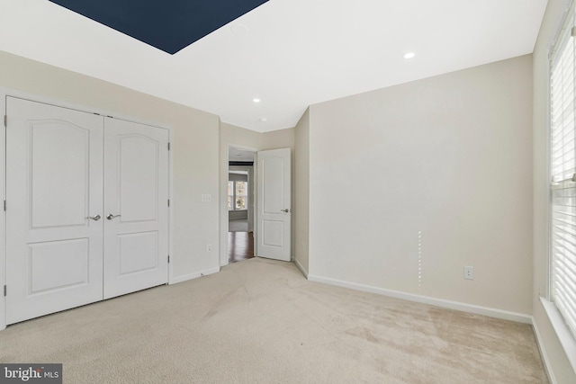 unfurnished bedroom featuring baseboards, a closet, recessed lighting, and light colored carpet