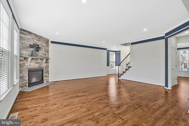 unfurnished living room with visible vents, ornamental molding, a stone fireplace, wood finished floors, and stairs