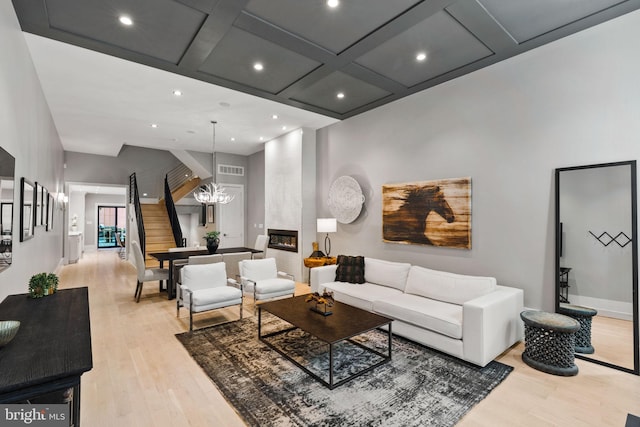 living area with light wood-style floors, a fireplace, visible vents, and coffered ceiling