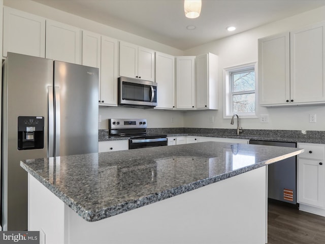 kitchen featuring a kitchen island, dark stone countertops, white cabinets, stainless steel appliances, and dark wood-style flooring