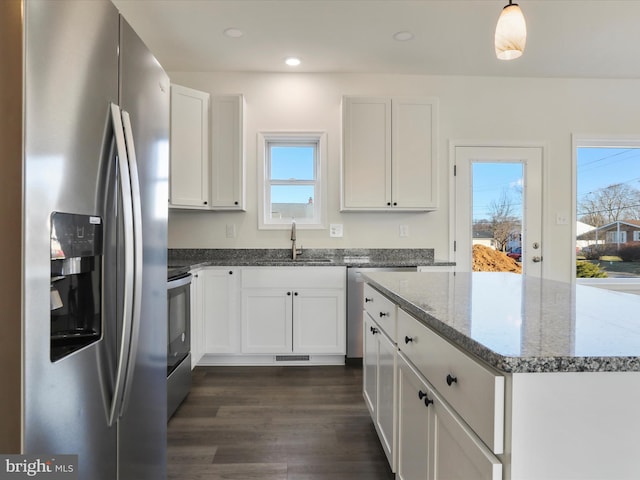 kitchen with a wealth of natural light, appliances with stainless steel finishes, dark stone counters, and a sink