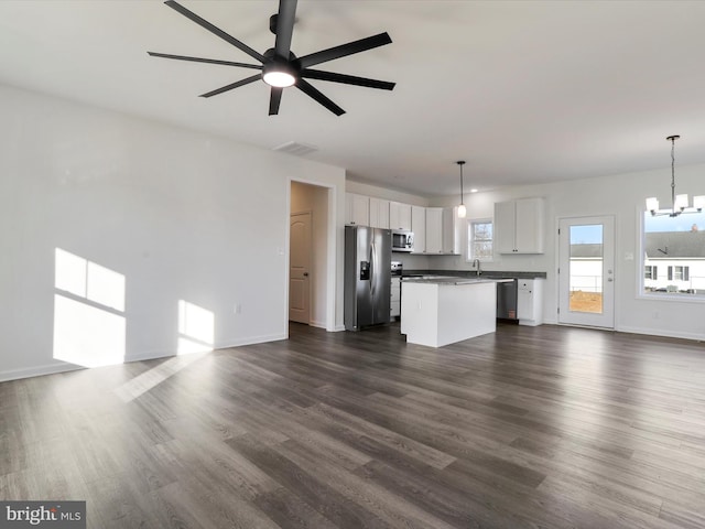 unfurnished living room featuring dark wood-style floors, visible vents, baseboards, a sink, and ceiling fan with notable chandelier