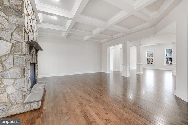 unfurnished living room featuring beamed ceiling, dark wood finished floors, a stone fireplace, and ornate columns