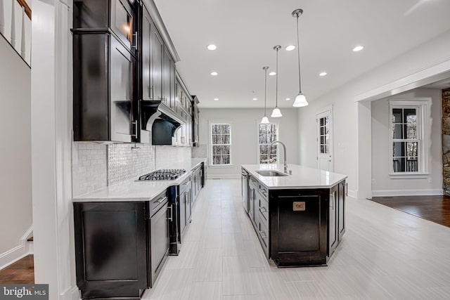 kitchen with decorative light fixtures, tasteful backsplash, light countertops, a sink, and an island with sink