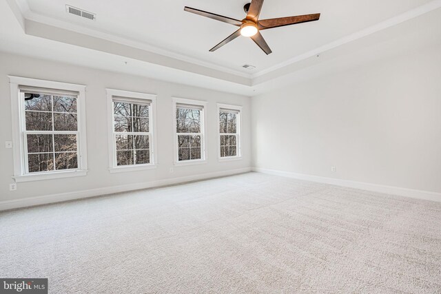 empty room with carpet floors, baseboards, a tray ceiling, and crown molding