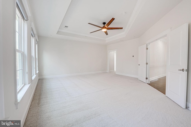 carpeted spare room with a tray ceiling, visible vents, ceiling fan, and baseboards