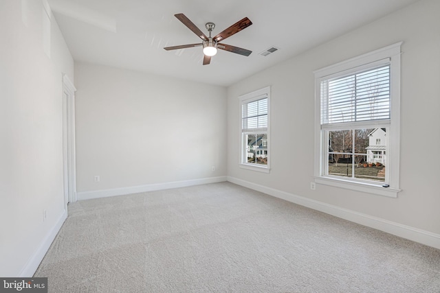 empty room featuring light colored carpet, visible vents, ceiling fan, and baseboards