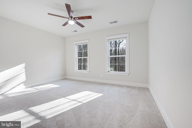 spare room with a ceiling fan, light colored carpet, visible vents, and baseboards