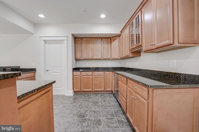 kitchen featuring glass insert cabinets, dark stone counters, brown cabinets, and recessed lighting