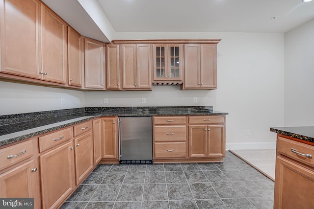 kitchen with dark stone countertops, fridge, glass insert cabinets, and baseboards