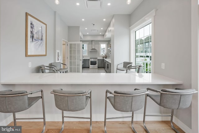 kitchen featuring a peninsula, wall chimney range hood, stainless steel range, and light countertops