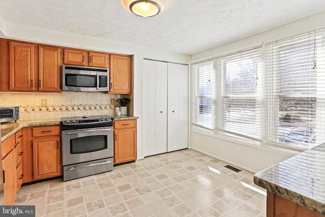 kitchen with brown cabinetry, tasteful backsplash, visible vents, and stainless steel appliances