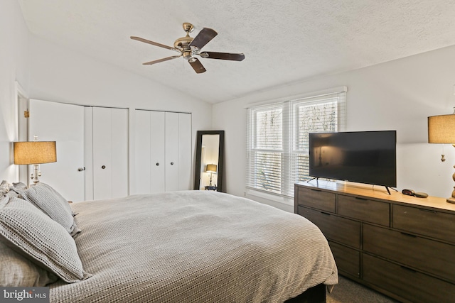 bedroom featuring lofted ceiling, a textured ceiling, a ceiling fan, and multiple closets