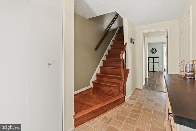 stairs with a textured ceiling, tile patterned flooring, and baseboards