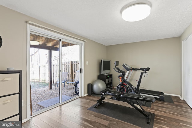 exercise area featuring a textured ceiling, baseboards, and wood finished floors