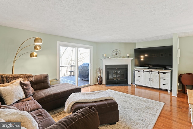 living area with a fireplace with flush hearth, a textured ceiling, and light wood finished floors