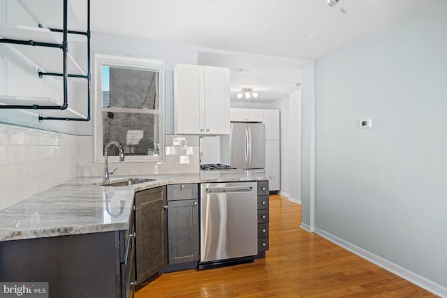 kitchen with stainless steel appliances, a sink, baseboards, light wood-type flooring, and backsplash