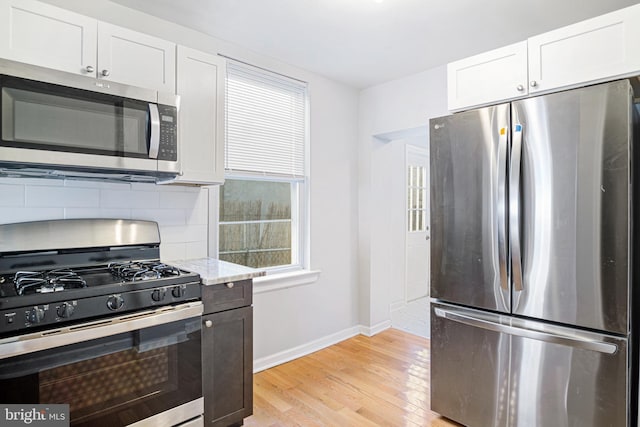 kitchen featuring white cabinetry, baseboards, light wood-style floors, appliances with stainless steel finishes, and backsplash