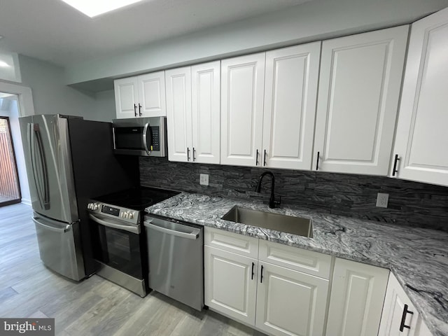 kitchen with white cabinets, light stone counters, stainless steel appliances, and a sink