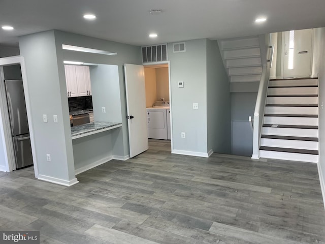 kitchen with light stone counters, stainless steel refrigerator, wood finished floors, washer and dryer, and white cabinetry