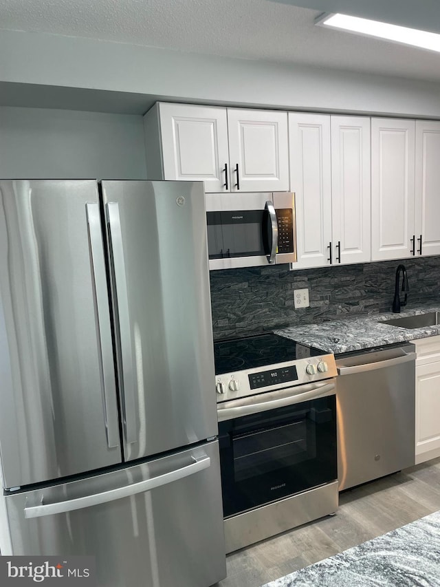 kitchen with light wood-style flooring, white cabinetry, stainless steel appliances, and a sink