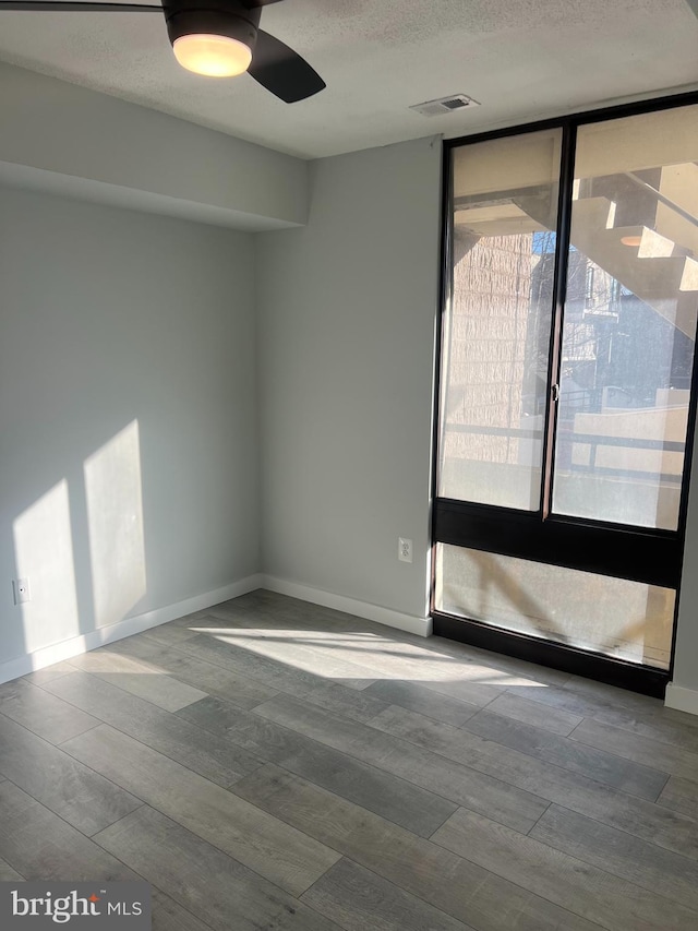 empty room featuring a wall of windows, wood finished floors, visible vents, and baseboards