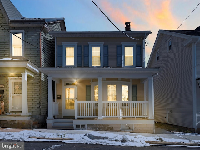 view of front of home with covered porch, brick siding, and a chimney