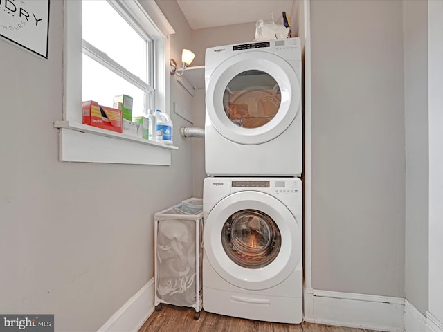 washroom featuring stacked washer and dryer, laundry area, baseboards, and wood finished floors