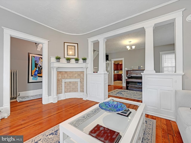 living room featuring a textured ceiling, wood finished floors, decorative columns, and radiator