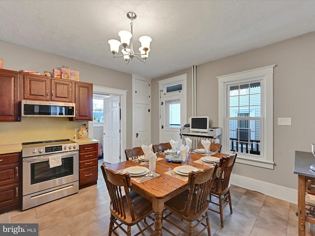 dining area with light tile patterned flooring, a textured ceiling, baseboards, and an inviting chandelier