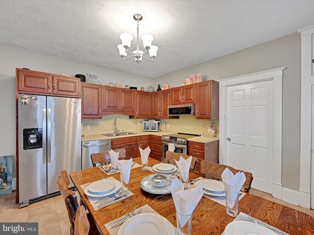 kitchen with an inviting chandelier, stainless steel appliances, light countertops, pendant lighting, and a sink