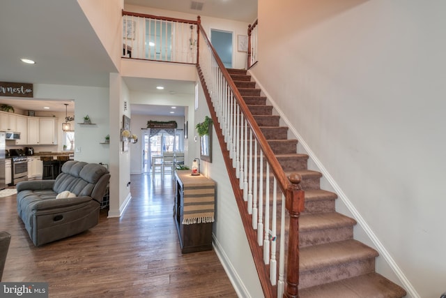 staircase with a towering ceiling, baseboards, wood finished floors, and recessed lighting