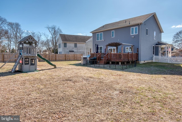 rear view of house featuring a deck, a playground, a lawn, and a fenced backyard