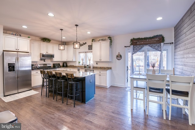 kitchen with a kitchen island, white cabinetry, hanging light fixtures, appliances with stainless steel finishes, and dark wood finished floors