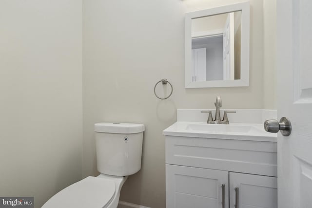 half bathroom with toilet, baseboards, and vanity