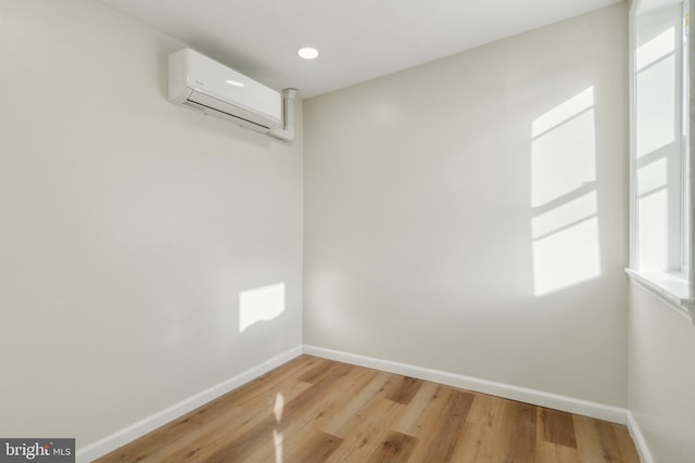 empty room with an AC wall unit, baseboards, and wood finished floors