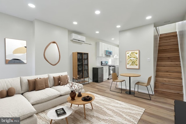 living area with recessed lighting, light wood-style floors, a wall mounted air conditioner, baseboards, and stairs