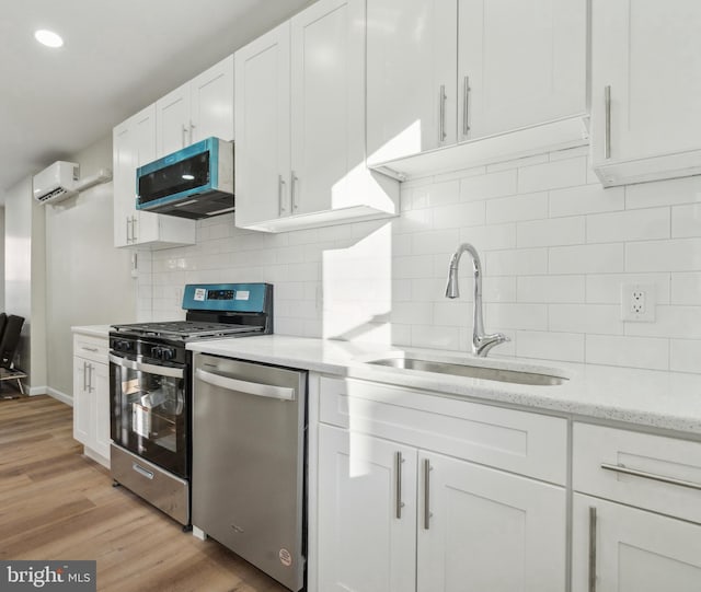 kitchen featuring a sink, light wood-style floors, white cabinets, appliances with stainless steel finishes, and light stone countertops