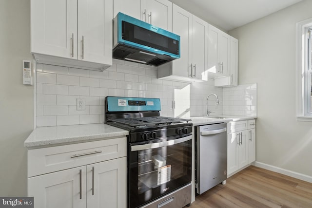 kitchen with stainless steel appliances, backsplash, light wood-style flooring, white cabinets, and a sink