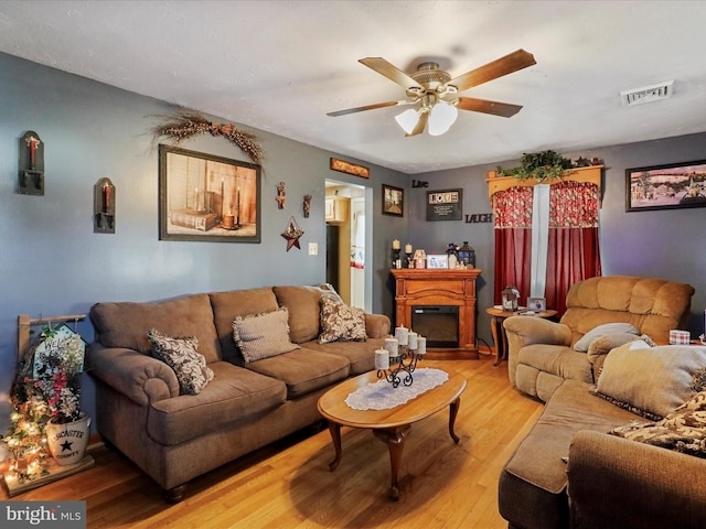 living room featuring ceiling fan, visible vents, wood finished floors, and a glass covered fireplace