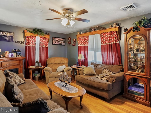 living room with ceiling fan, visible vents, and wood finished floors