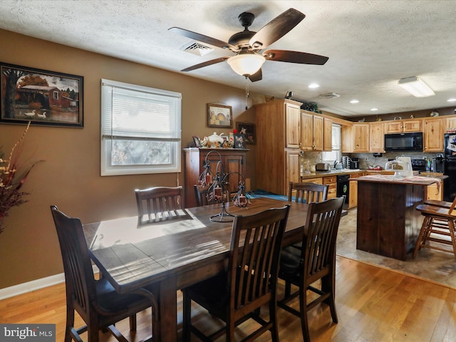 dining area with light wood-style floors, visible vents, a textured ceiling, and baseboards