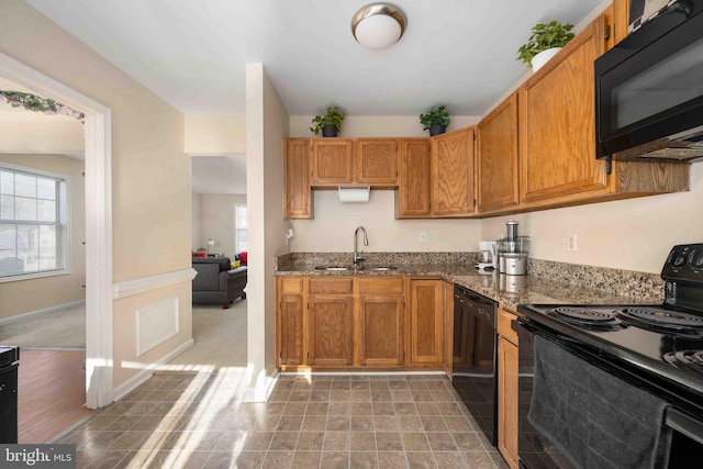 kitchen with black appliances, stone counters, a sink, and brown cabinets