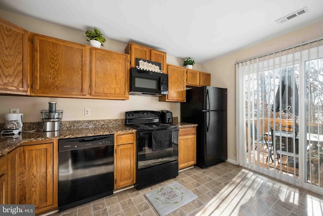 kitchen featuring visible vents, baseboards, brown cabinets, dark stone counters, and black appliances