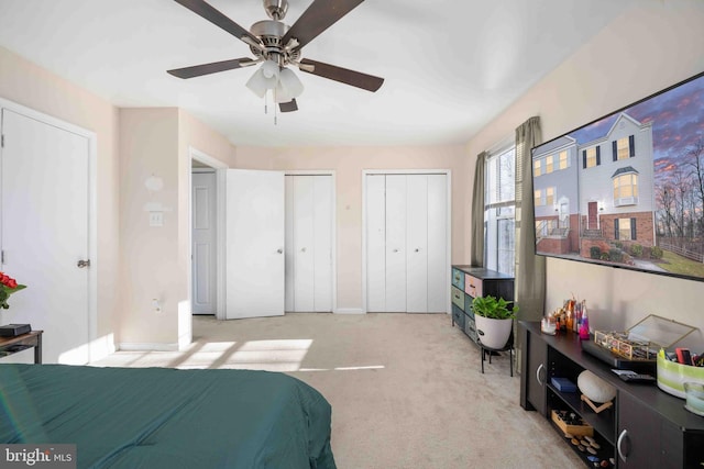 bedroom featuring ceiling fan, multiple closets, baseboards, and light colored carpet